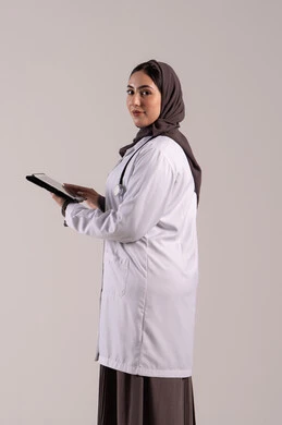 مفهوم الطب والرعاية الصحية, تطور القطاع الصحي في الامارات العربية،  سيده سعودية تقوم بتقديم الاستشارات للمرضى عن بعد الأجهزة التكنولوجية، بورتريه لطبيبة عربية خليجية اماراتية ترتدي المعطف الأبيض و السماعة تمسك جهاز التابلت ، خلفية بنية