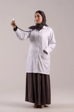مفهوم الطب و الرعاية، بورتريه لطبيبة عربية خليجية اماراتية محجبة ترتدي المعطف الطبي وتحمل بيدها سماعة الطبيب لسماع نبضات القلب, سيده سعودية تعمل في مجال الرعاية الصحية وتقديم الخدمات الطبية المتميزة، الجسم بالطول الكامل, خلفية بنية