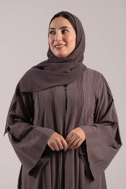 مفهوم الانوثة والاناقة, شابة سعودية انيقة، ايماءات السرور والسعادة، الاهتمام بالمظهر الخارجي، بورتريه لامرأه عربيه خليجيه اماراتيه مبتسمة ترتدي عباءة تنظر إلى شيء ما, خلفية بنية