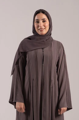 شابة سعودية انيقة، ايماءات السرور والسعادة، الاهتمام بالمظهر الخارجي، مفهوم الانوثة والاناقة، بورتريه لامرأه عربيه خليجيه اماراتيه مبتسمة ترتدي عباءة تنظر إلى الكاميرا بتعابير الفرح, خلفية بنية