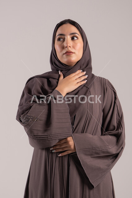 الانفلونزا والتهاب الرئة, الشعور بالمرض والكحة، تعابير الالم والارهاق، بورتريه لامرأة عربية خليجية اماراتية محجبة ترتدي عباءة تضع يدها حنجرتها بايماءات التوجع، شابة سعودية مريضة، خلفية بنية