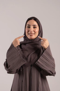 إشارات وحركات يدين تدل على هذا المكان (هنا)، تحديد موقع شيء معين، بورتريه لامرأة عربية خليجية اماراتية محجبة ترتدي عباءة تشير بإصبع السبابة إلى وجهها، شابة سعودية انيقة، خلفية بنية