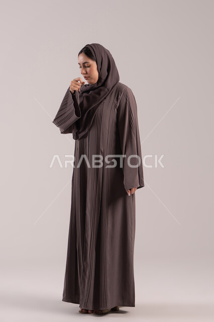 الشعور بالمرض والكحة، الاصابة بفايروس كورونا كوفيد19، الانفلونزا والتهاب الرئة، بورتريه لامرأه عربية خليجية اماراتية محجبة ترتدي عباءة تعاني من السعال، شابة سعودية مريضة، الجسم بالطول الكامل, خلفية بنية