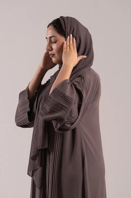 الحاجة للهدوء والراحة، الإحساس بألم الرأس والصداع، المعاناة من آلام الشقيقة، بورتريه من الجانب لإمرأة عربية خليجية اماراتية محجبة ترتدي عباءة تضع يديها على رأسها بايماءات التعب والارهاق، شابة سعودية مريضة، صورة الجسم بالطول الكامل، خلفية بنية