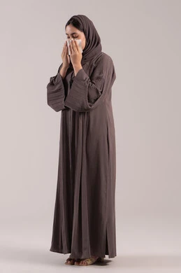 التعرض للإصابة بفيروس كوفيد-19, استعمال المناديل الورقية أثناء العطس، الشعور بالتعب والمرض، بورتريه لامرأه عربيه خليجيه اماراتية محجبة ترتدي عباءة ، إيماءات وجه ويدين تدل على العطاس، شابة سعودية مريضة، الجسم بالطول الكامل, خلفية بنية