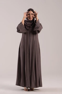 مفهوم الرؤية المستقبلية, حب البحث والاستكشاف والمغامرة، بورتريه لامرأة عربية خليجية إماراتية محجبة مبتسمة ترتدي عباءة سوداء تحاول تقريب الأشياء البعيدة, سيدة سعودية تضع يديها على عينها بشكل عدسة, الجسم بالطول الكامل . خلفية بنية