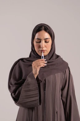 شعور بالتعب المصحوب بالحمى، وضع خطة علاجية، الحاجة للمساعدة وزيارة الطبيب، الإحساس بالمرض والإرهاق، بورتريه لامرأة عربية خليجية اماراتية محجبة ترتدي عباءة تقوم بقياس حرارتها باستخدام الميزان الرقمي، شابة سعودية مريضة، خلفية بنية