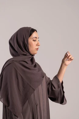 General fatigue accompanied by illness, following safety and prevention procedures, the need to visit a doctor and establish a treatment plan, suffering from fever and fatigue, a side portrait of an Emirati Gulf Arab woman wearing a hijab and an abaya holding a digital thermometer in her hand, a sick young Saudi woman, brown background.