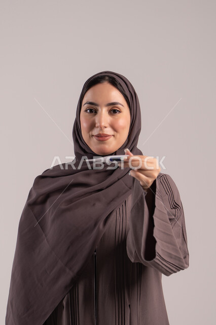 الشعور بالتعب والمرض, اتباع إجراءات السلامة والوقاية، الحاجة لزيارة الطبيب ووضع خطة علاجية، الإصابة بالحمى والتعب، بورتريه لامرأة عربية خليجية اماراتية محجبة ترتدي عباءة تحمل بيدها ميزان حرارة رقمي، شابة سعودية مريضة، خلفية بنية