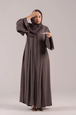 الإحساس بالمرض والإرهاق, الحاجة للمساعدة وزيارة الطبيب، الإصابة بالحمى والتعب، بورتريه لامرأة عربية خليجية اماراتية محجبة ترتدي عباءة سوداء تضع يدها على جبينها تقوم بقياس حرارتها باستخدام الميزان الرقمي، وضع خطة علاجية، شابة سعودية مريضة،الجسم بالطول الكامل, خلفية بنية