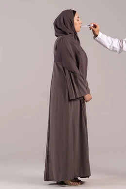 وضع خطة علاجية, الإحساس بالمرض والإرهاق، الإصابة بالحمى والتعب، بورتريه من الجانب لامرأة عربية خليجية اماراتية محجبة ترتدي عباءة  تقوم بقياس حرارتها باستخدام الميزان الرقمي، الحاجة للمساعدة وزيارة الطبيب، شابة سعودية مريضة،  الجسم بالطول الكامل, خلفية بنية