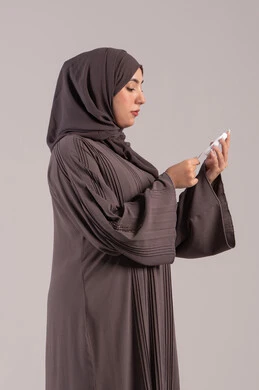 جهاز طبي إلكتروني مخصص لمرضى السكري,مشاكل ارتفاع السكر في الدم, حالات مرضية ومشاكل وآلام جسدية, الرعاية الصحية والفحص الطبي السريع, بورتريه من الجانب لامرأة عربية خليجية إماراتية تقوم بفحص نسبة السكر في الدم, شابة سعودية مريضة، خلفية بنية