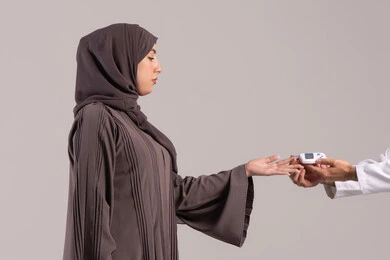 التحكم في سكر الدم من خلال أجهزة قياس منزلية، بورتريه مقرب ليد ممرض يرتدي اليونيفورم يقوم بفحص نسبة السكر في الدم لمريضة عربية خليجية إماراتية ترتدي العباءة، شركات الرعاية الصحية المنزلية، فحص طبي سريع في البيت، خلفية بنية