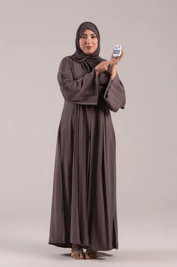 Medical conditions, problems, and physical pains, issues with high blood sugar, a modern electronic device for diabetes patients, healthcare and rapid medical testing, a portrait of an Emirati Gulf Arab woman checking her blood sugar level, a sick young Saudi woman, full-body, brown background.