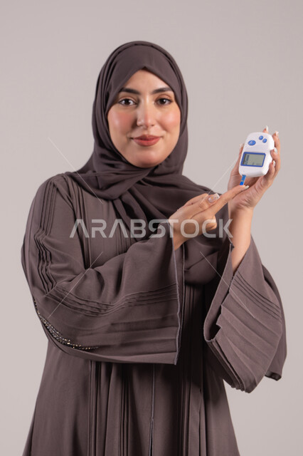 مشاكل ارتفاع السكر في الدم, جهاز إلكتروني حديث لمرضى داء السكري, حالات مرضية ومشاكل وآلام جسدية, الرعاية الصحية والفحص الطبي السريع, بورتريه لامرأة عربية خليجية إماراتية تقوم بفحص نسبة السكر في الدم, شابة سعودية مريضة، خلفية بنية
