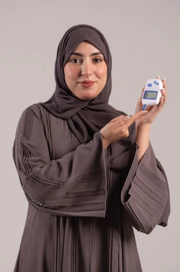 مشاكل ارتفاع السكر في الدم, جهاز إلكتروني حديث لمرضى داء السكري, حالات مرضية ومشاكل وآلام جسدية, الرعاية الصحية والفحص الطبي السريع, بورتريه لامرأة عربية خليجية إماراتية تقوم بفحص نسبة السكر في الدم, شابة سعودية مريضة، خلفية بنية