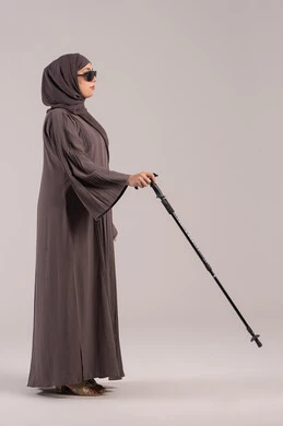 اعتماد الشخص الضرير على العصا بشكل كامل في جميع تحركاته, فقدان الرؤية والبصر, مفهوم الصحة والمرض, بورتريه من الجانب لامرأة عربية خليجية اماراتية كفيفه مصابة بالعمى ترتدي النظارة الشمسية و بيدها العكاز، الجسم بالطول الكامل, خلفية بنية