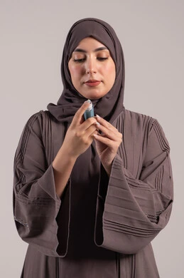 معاناة من مشاكل صدرية وتنفسية, شابة سعودية مريضة، المحافظة على ممر هوائي منتظم، بورتريه لامرأة عربية خليجية اماراتية محجبة ترتدي عباءة تحمل بيدها جهاز الرذاذ الخاص بمرض الربو تقوم باستنشاق أدوية الكحة، صورة ، خلفية بنية