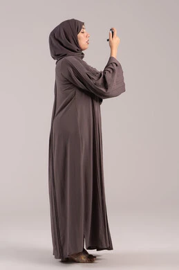 شابة سعودية مريضة، المحافظة على ممر هوائي منتظم، مشاكل في الجهاز التنفسي، بورتريه من الجانب لامرأة عربية خليجية اماراتية محجبة ترتدي عباءة تحمل بيدها جهاز الرذاذ الخاص بمرض الربو تقوم باستنشاق أدوية الكحة، صورة الجسم بالطول الكامل، خلفية بنية