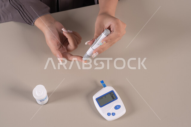 A sick young Saudi woman, a modern electronic device for diabetes patients, medical conditions and problems and physical pains, a vertical overhead portrait of an Emirati Gulf Arab woman checking her blood sugar level, healthcare and rapid medical examination, problems of high blood sugar, brown background.
