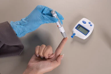 مشاكل ارتفاع السكر في الدم, جهاز إلكتروني حديث لمرضى داء السكري, حالات مرضية ومشاكل وآلام جسدية, بورتريه علوي عامودي ليد امرأة عربية خليجية إماراتية ترتدي قفازات الوقاية تقوم بفحص نسبة السكر في الدم, الرعاية الصحية والفحص الطبي السريع, شابة سعودية مريضة، خلفية بنية