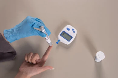 Healthcare and rapid medical examination, a modern electronic device for diabetes patients, medical conditions and problems and physical pains, a vertical overhead portrait of the hand of an Emirati Gulf Arab woman wearing protective gloves checking blood sugar levels, problems of high blood sugar, a sick Saudi young woman, brown background.