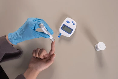 جهاز إلكتروني حديث لمرضى داء السكري, حالات مرضية ومشاكل وآلام جسدية, بورتريه علوي عامودي ليد امرأة عربية خليجية إماراتية ترتدي قفازات الوقاية تقوم بفحص نسبة السكر في الدم, الرعاية الصحية والفحص الطبي السريع, مشاكل ارتفاع السكر في الدم, شابة سعودية مريضة، خلفية بنية