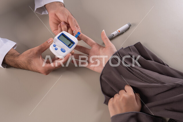 مراقبة مستوى السكر في الدم عبر أجهزة منزلية، بورتريه مقرب ليد ممرض يرتدي اليونيفورم يقوم بفحص نسبة السكر في الدم لمريضة عربية خليجية إماراتية ترتدي العباءة، شركات الرعاية الصحية المنزلية، فحص طبي سريع في البيت، خلفية بنية