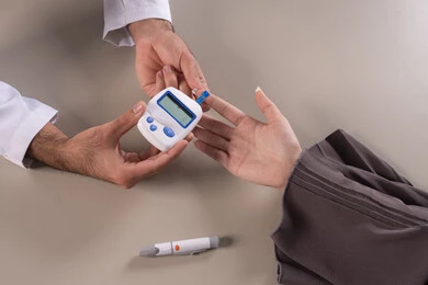 فحص نسبة السكر بالمنزل لمرضى السكري، بورتريه مقرب ليد ممرض يرتدي اليونيفورم يقوم بفحص نسبة السكر في الدم لمريضة عربية خليجية إماراتية ترتدي العباءة، خدمات التمريض المنزلي، رصد ومتابعة طبية سريعة، خلفية بنية