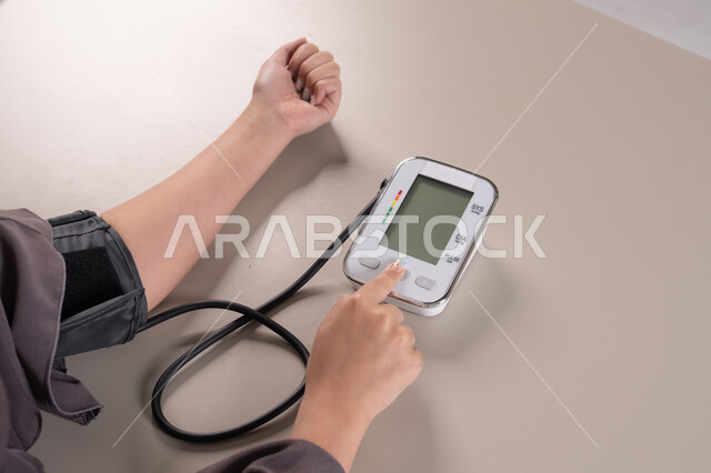 استخدام الميزان الاكتروني الحديث والمتطور للفحص المنزلي السريع , العناية والاهتمام والحفاظ على الصحة, المتابعة الدورية لفحص الدم, بورتريه مقرب ليد امراة عربية خليجية  اماراتية ترتدي العباءه تقوم بقياس ضغط الدم , مفهوم الطب والرعاية الصحية, خلفية بنية