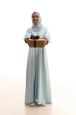 Looking with gestures of joy and happiness, holidays, occasions, and happy surprises, the joy of receiving a gift and congratulations, a portrait of a Saudi Arabian Gulf woman wearing a hijab and an abaya, holding a wrapped box in her hands, full-body image, white background.