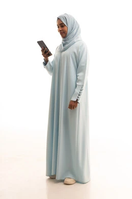 الدردشة مع الأهل والأصدقاء، إيماءات السعادة والسرور، استخدام الاجهزة التقنية الحديثة، بورتريه من الجانب لامرأة عربية خليجية سعودية محجبة تحمل بيدها الهاتف المحمول، تصفح وسائل التواصل الاجتماعي، الجسم بالطول الكامل، خلفية بيضاء