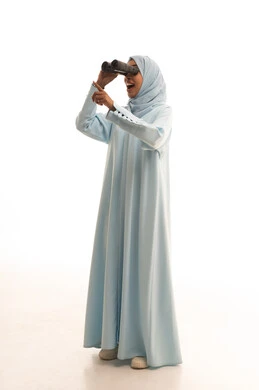 Seeing distant things through a telescope, pointing to something, future planning for goals and ambitions, love of exploration and adventure, a portrait of a Saudi Arabian Gulf woman wearing a hijab and abaya looking through binoculars, full body, white background.