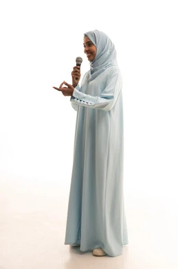 ايماءات وتعابير وجه و يدين تعبر عن الغناء والطرب، فن إلقاء الخطابات والندوات، التدريب الصوتي وتقديم البرامج الاذاعيه، بورتريه لشابة عربية خليجية سعودية ترتدي العباءة و الحجاب تمسك بيدها الميكروفون، الجسم بالطول الكامل، خلفية بيضاء