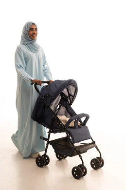 مفهوم الأمومة والرعايه والاهتمام بالأولاد، أهمية الأم ودورها الأساسي في تربية ونشأة الأبناء, بورتريه لأم عربية خليجيه سعودية ترتدي العباءة و الحجاب تقوم بجر عربة الأطفال, ايماءات السعادة والسرور، القيام بالنزهات والجولات العائلية، الجسم بالطول الكامل، خلفية بيضاء