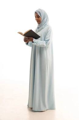 The concept of self-learning, gestures of contemplation and focus, spending time reading, learning, and culture, a portrait of an Arab Gulf Saudi woman wearing an abaya and hijab reading a book, full-body, white background.