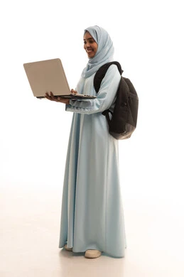المواد والمناهج التعليمية في المملكة، مفهوم التعليم عن بعد، استخدام الأجهزة التقنية الحديثة لمتابعة المحاضرات، بورتريه من الجانب لطالبة جامعية عربية خليجية سعودية محجبة ترتدي عباءة تحمل حقيبة الظهر والحاسوب المحمول، الجسم بالطول الكامل، خلفية بيضاء