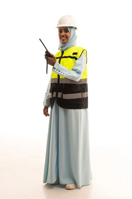 الإشراف على المشاريع، مراقبة سير العمل، العمل في القطاع الهندسي، بورتريه لمهندسة عربية خليجية سعودية ترتدي سترة وخوذة الحماية تقوم باستخدام جهاز الاتصال اللاسلكي، مهن وظائف هندسية، الجسم بالطول الكامل، خلفية بيضاء