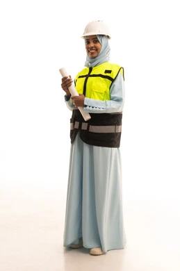النظر للكاميرا بتعابير السعادة و السرور، مفهوم دراسة المخطط والمشروع البناء، مهنة ووظيفة هندسية نسائية ، بورتريه لمهندسة عربية خليجية سعودية ترتدي العباءة والسترة وخوذة الحماية تمسك بيديها المخطط ، العمل في القطاع الهندسي في المملكة العربية السعودية، خلفية بيضاء