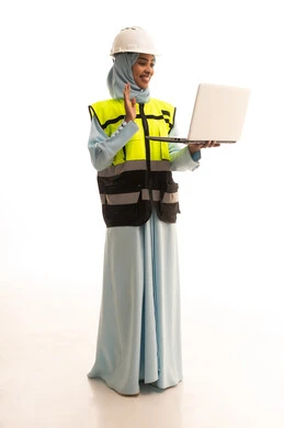 Making a video call over the internet, raising a hand with expressions of peace and greeting, completing work tasks via a laptop, managing engineering projects, a portrait of an Arab Gulf Saudi engineer wearing a jacket and safety helmet holding a laptop, working in the engineering sector, full-body image, white background.