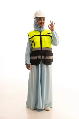 مفهوم الانشاءات المعمارية والهندسة، جودة الفن في تقنية التصميم والبناء، بورتريه لمهندسة عربية خليجية سعودية مبتسمة ترتدي الخوذه و سترة الحماية تشير بيديها  للأعلى بعلامه الجوده، الجسم بالطول الكامل، خلفية بيضاء