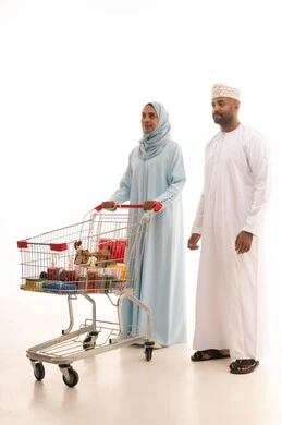 النظربإيماءات  السعادة والسرور، شراء المنتجات من السوبر ماركت، التجول في المول والمركز التجاري، بورتريه من الجانب لامراة عربيه خليجيه عمانية ترتدي العباءة و الحجاب تقوم بجرعربة التسوق برفقة زوجها، المشاركة في شراء المستلزمات المنزلية، الاستفادة من الخصومات والعروض، الجسم بالطول الكامل، خلفية بيضاء
