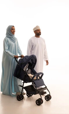 Going on a family tour, caring for and paying attention to the children, an Omani family having a good time, the importance of parents and their essential role in raising children, a portrait of an Arab Gulf Omani woman wearing a hijab and abaya standing with her husband pulling a baby stroller, white background.