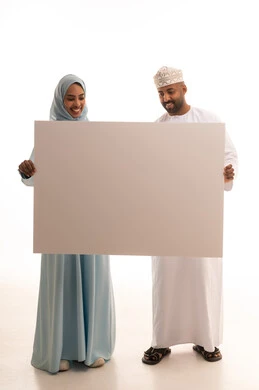 Using illustrative boards and educational tools, advertisements and marketing presentations, a portrait of an Arab Gulf Omani man wearing a dishdasha and a kumma holding a large white board (empty mock-up) accompanied by his wife, gestures of happiness and joy, full body length, white background.