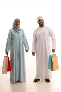 Looking at the camera with gestures of happiness and joy, the couple participating in choosing purchases, benefiting from discounts and seasonal offers, having a good time shopping on Black Friday, a portrait of an Arab Gulf couple from Oman holding colorful shopping bags, full body length, white background.