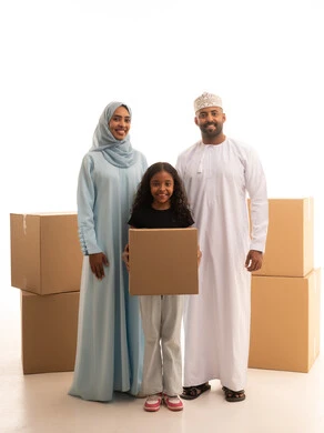 النظر للكاميرا بايماءات السعادة والسرور، مفهوم امتلاك سكن جديد والاستقرار العائلي، بورترية لبنت عربيه خليجيه عمانية ترتدي الزي الكاجوال تحمل صندوق كرتوني برفقة والديها ، خلفية بيضاء