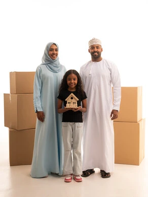 صناديق وحاويات كرتونية، ايماءات السعادة والسرور، مفهوم امتلاك سكن جديد والاستقرار العائلي، بورترية لبنت عربيه خليجيه عمانية ترتدي الزي الكاجوال تحمل مجسم خشب لبيت صغيربرفقة والديها ، خلفية بيضاء