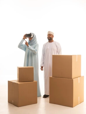 مفهموم امتلاك سكن جديد والاستقرار العائلي، بورترية لامراه عربيه خليجيه عمانية ترتدي العباءه و الحجاب و نظارة الواقع الإفتراضي ثلاثية الأبعاد برفقة زوجها ، النقل الى منزل جديد،الاشارة الى شيء ما، صورة الجسم بالطول الكامل، خلفية بيضاء