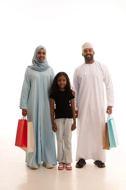 Looking at the camera with gestures of happiness and joy, taking advantage of discounts and seasonal offers, shopping for global products, enjoying shopping and buying items during Black Friday, a portrait of an Arab Gulf couple from Oman carrying colorful shopping bags with their daughter, full body length, white background.