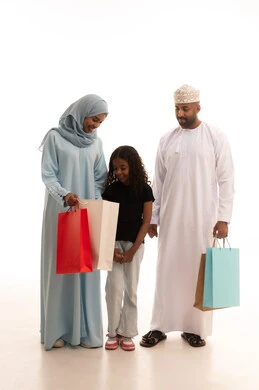 Exploiting discounts and seasonal offers, shopping for global products, enjoying shopping and buying items during Black Friday, a portrait of an Arab Gulf couple from Oman carrying colorful shopping bags with their daughter, full body length, white background.